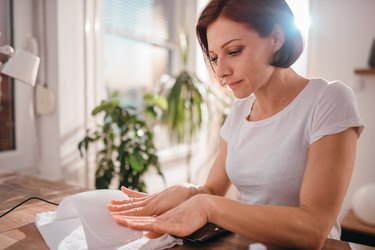 Person with chin-length brown hair wearing a white t-shirt and looking for signs of a vitamin deficiency in their nails