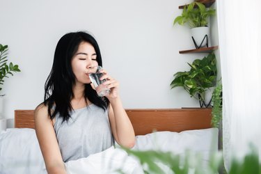 a person drinking a glass of water in bed after waking up dizzy