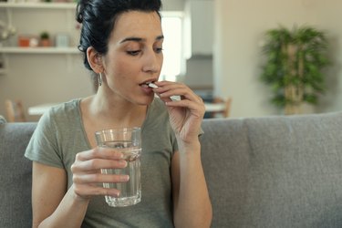 Person with black hair wearing a green t-shirt and sitting on their couch taking iron pills because their iron is level 5