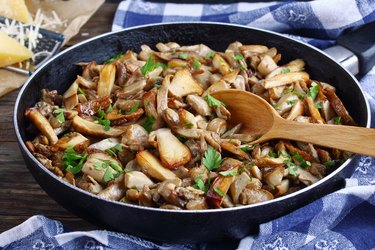 a wooden spoon rests in a skillet of porcini mushrooms with parsley as an example of what to eat when sick