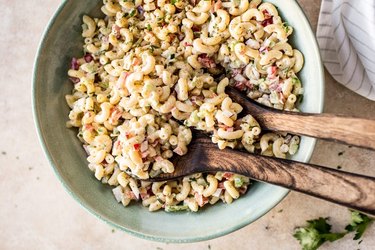 an overhead photo of a light green bowl of Classic Macaroni Salad with two wooden serving spoons