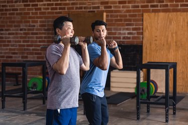 Personal trainer showing person how to lift dumbbells in gym.