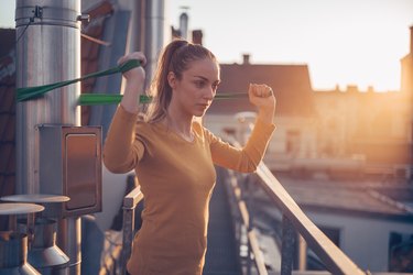 Gym-goer working out with resistance bands on roof of apartment