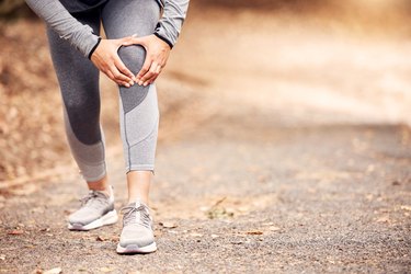 Woman experiencing knee clicking while running outside in nature