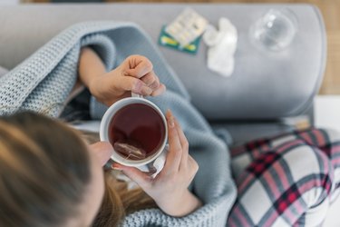 Woman drinking tea while suffering from a cold or a fever.