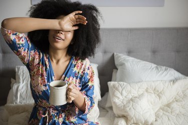 African American woman sitting in bed drinking coffee